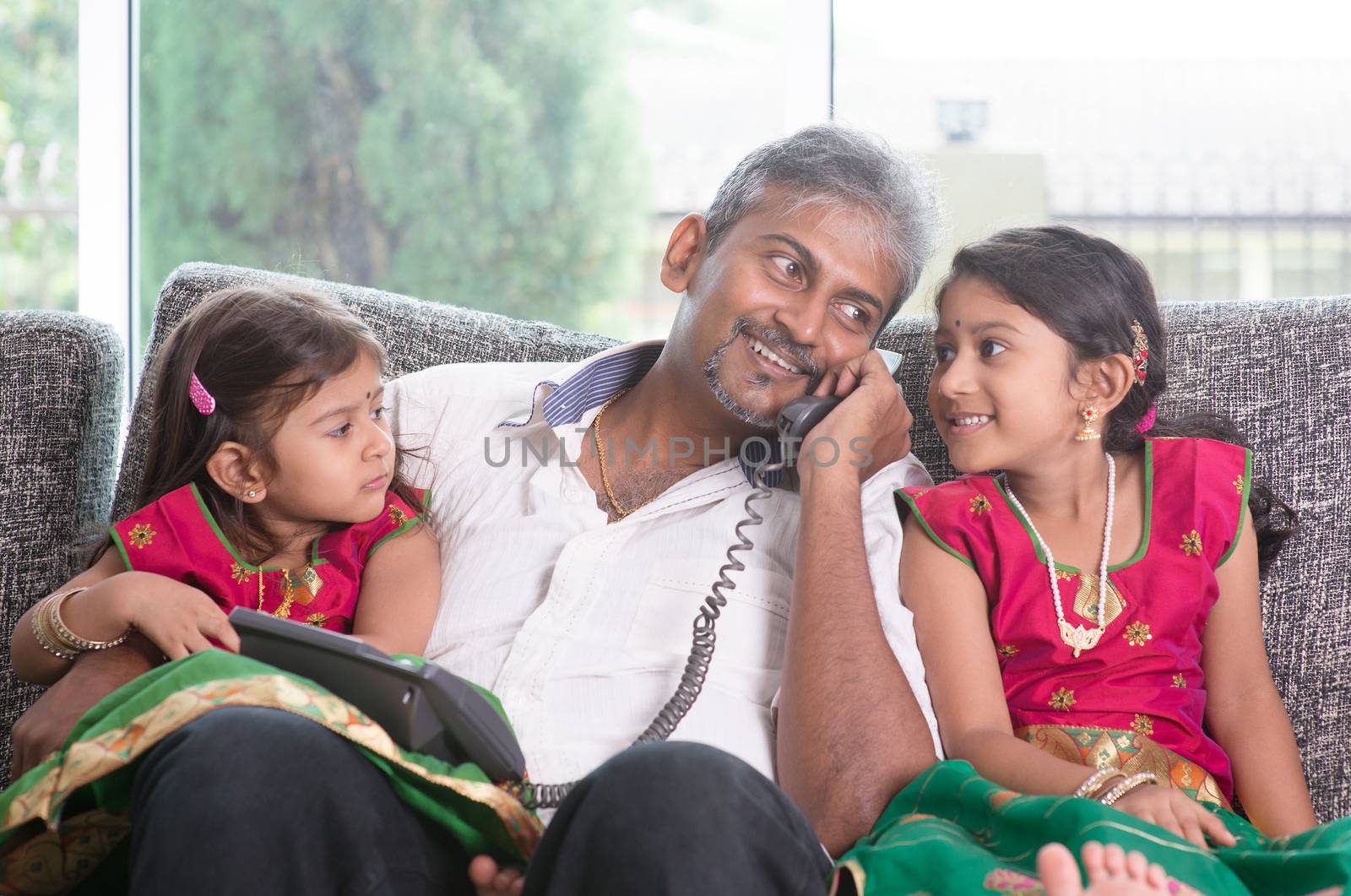 Husband making a phone call to wife while taking care of children at home. Asian Indian family at home.