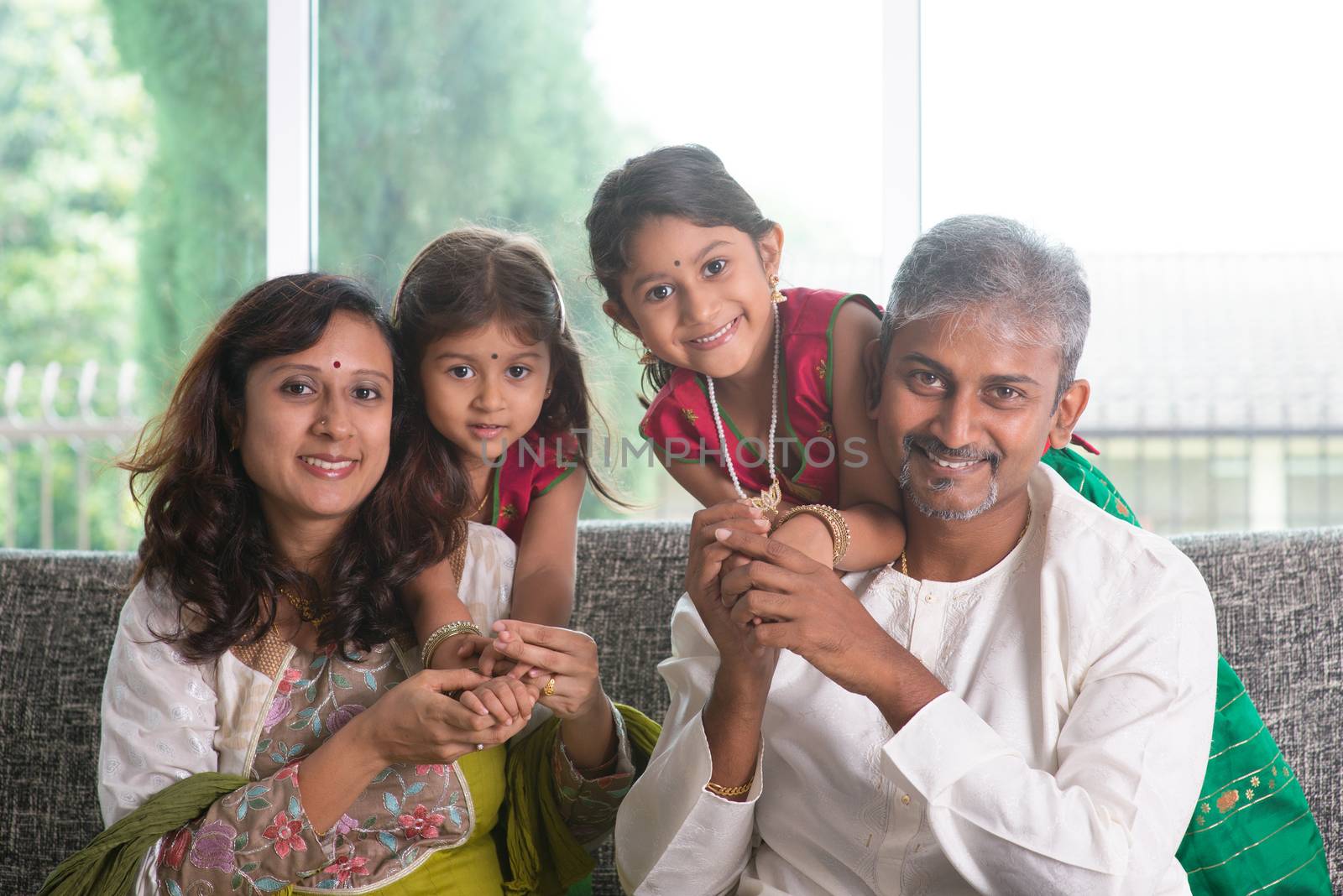 Happy Indian family at home. Asian parents with their kids, sitting on sofa. Parents and children indoor lifestyle.