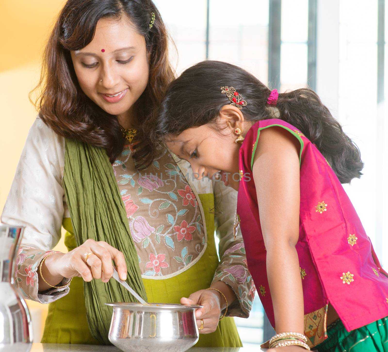 Asian family cooking food together at home. Indian mother and child preparing meal in kitchen. Traditional India people with sari clothing.