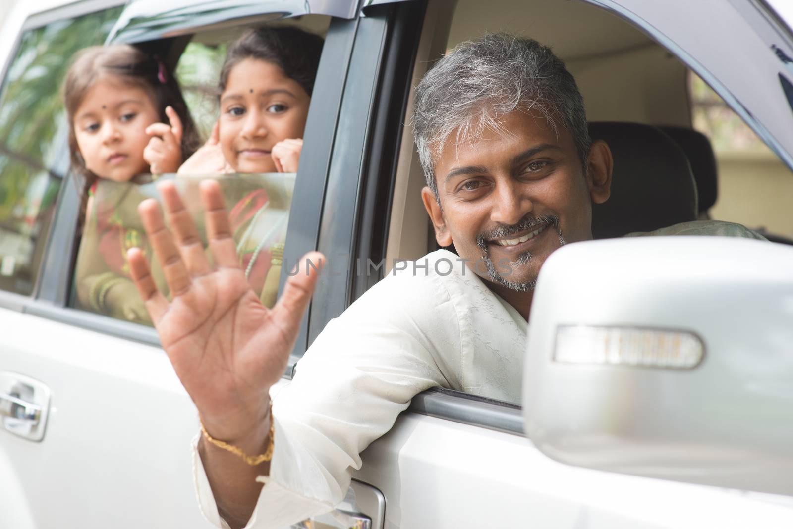 Indian family waving hands and saying goodbye, sitting in car ready to trip. Asian family lifestyle.