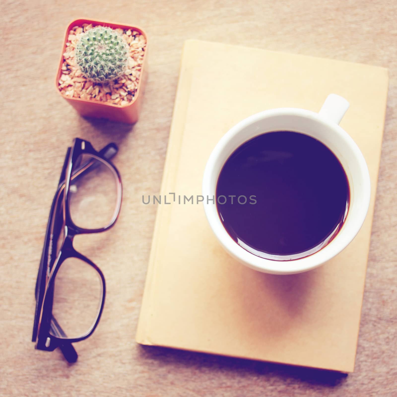 Black coffee on notebook and cactus with eyeglasses, retro filter effect