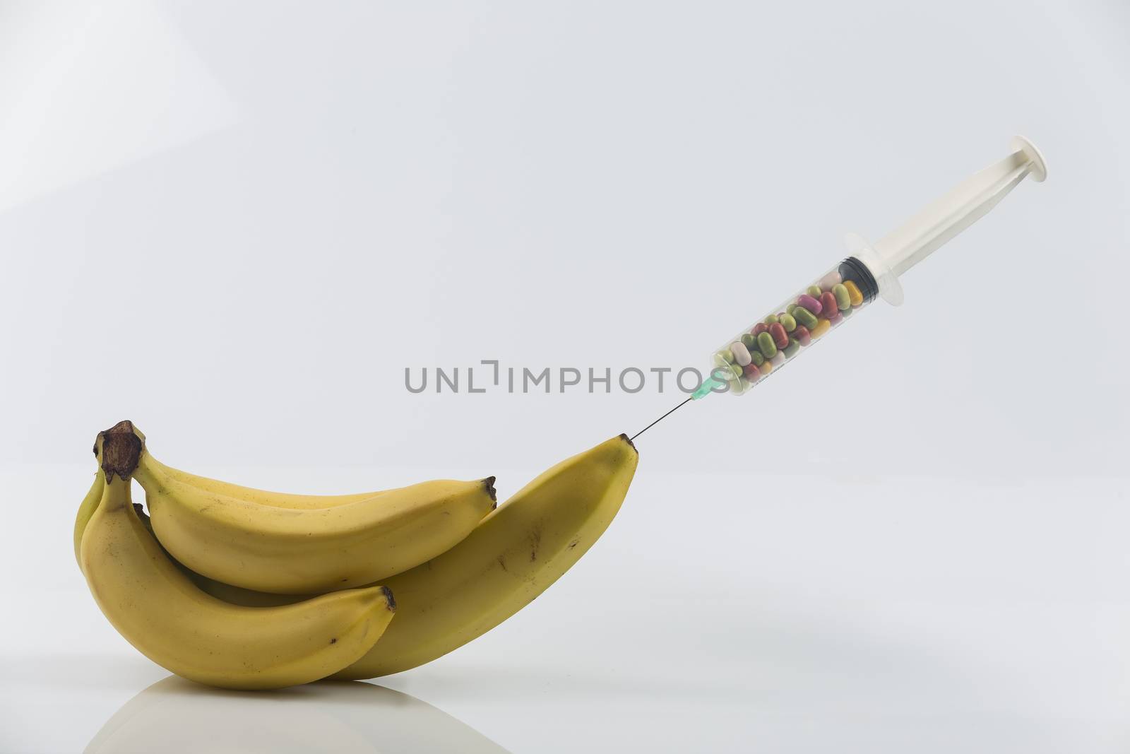 Male impotence metaphor: syringe with pills injecting into a  big banana among small bananas