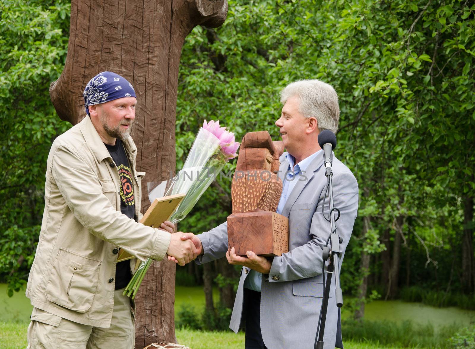 JUKNENAI, LITHUANIA - JUNE 09: presenter shake hands with prize winner and give flowers and wooden sculpture on June 09, 2013 in Juknenai.