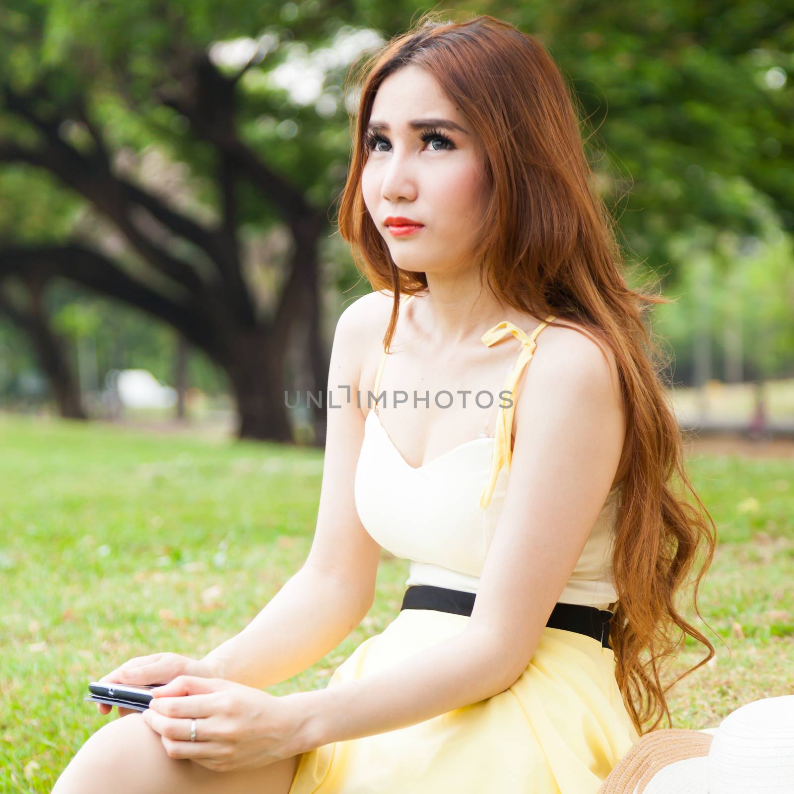 Woman sitting on lawn Hand holding tablet and thinking.