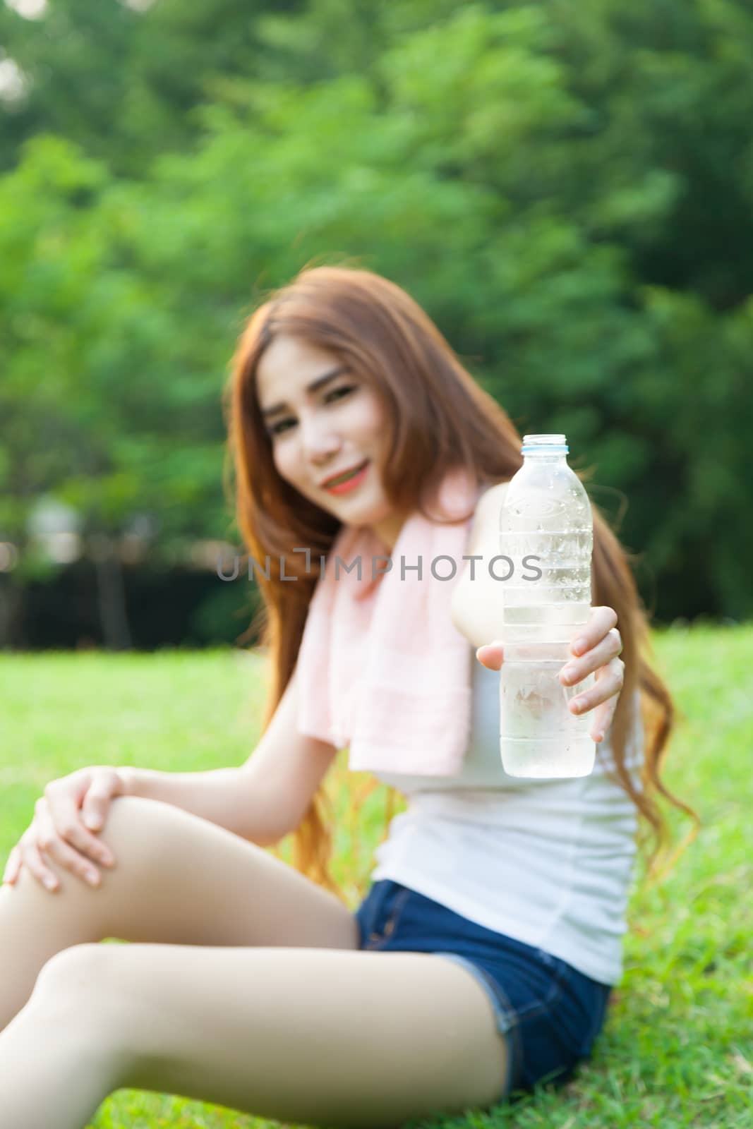 Women held a water bottle to drink. Sit on the lawn after exercise in park.