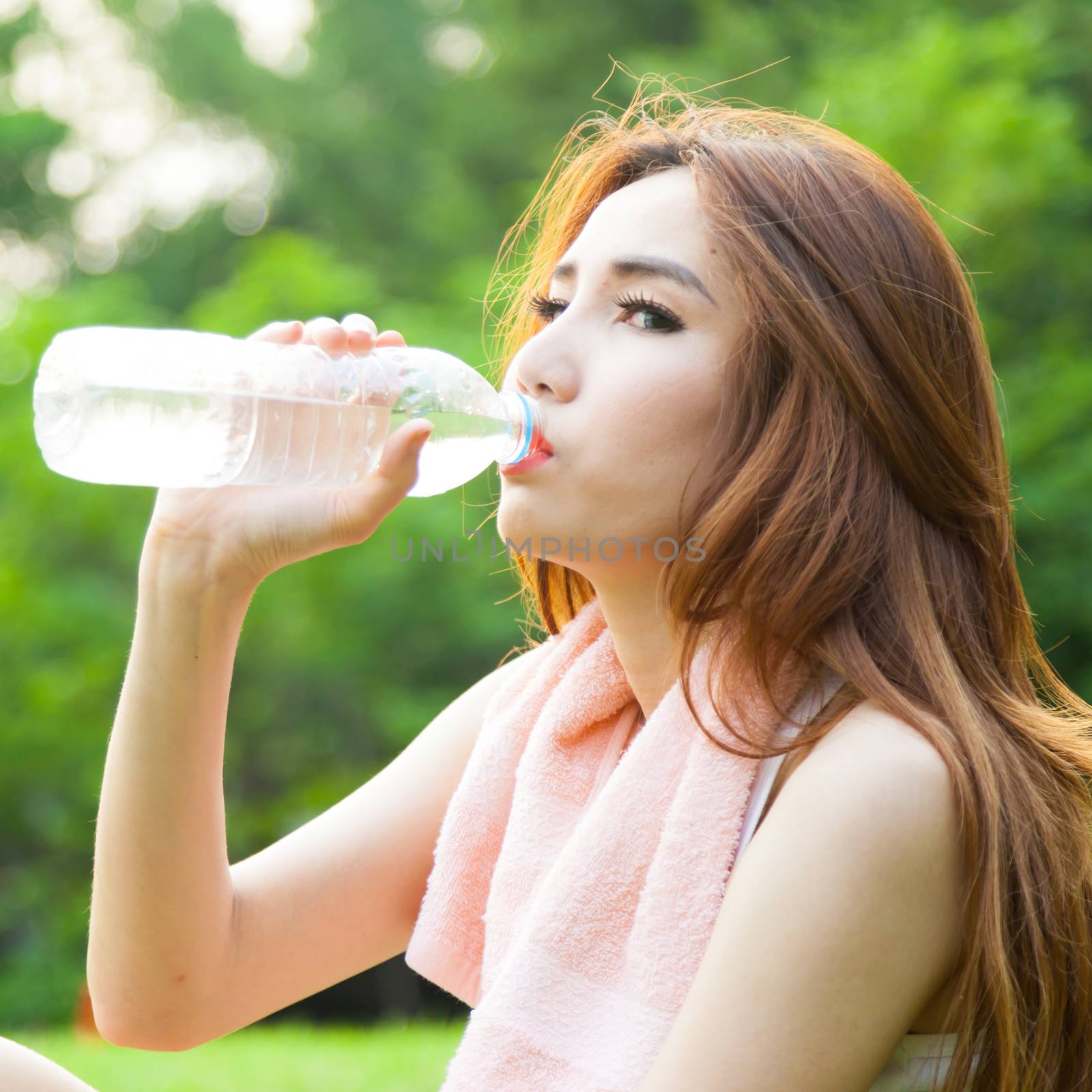 Woman sitting tired and drinking water after exercise. Within the lawn of park.