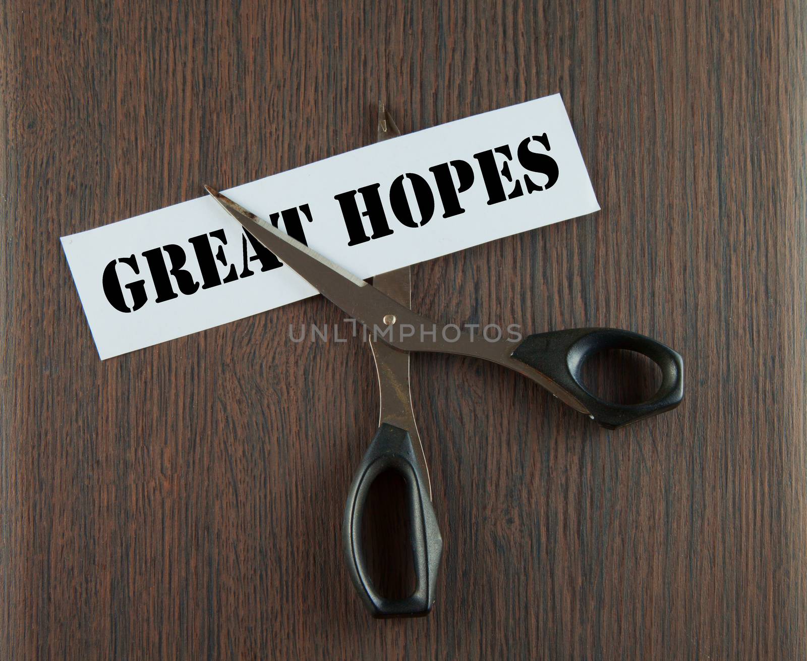 Scissors cutting the words "Great Hopes" written on a paper strip, over wooden background