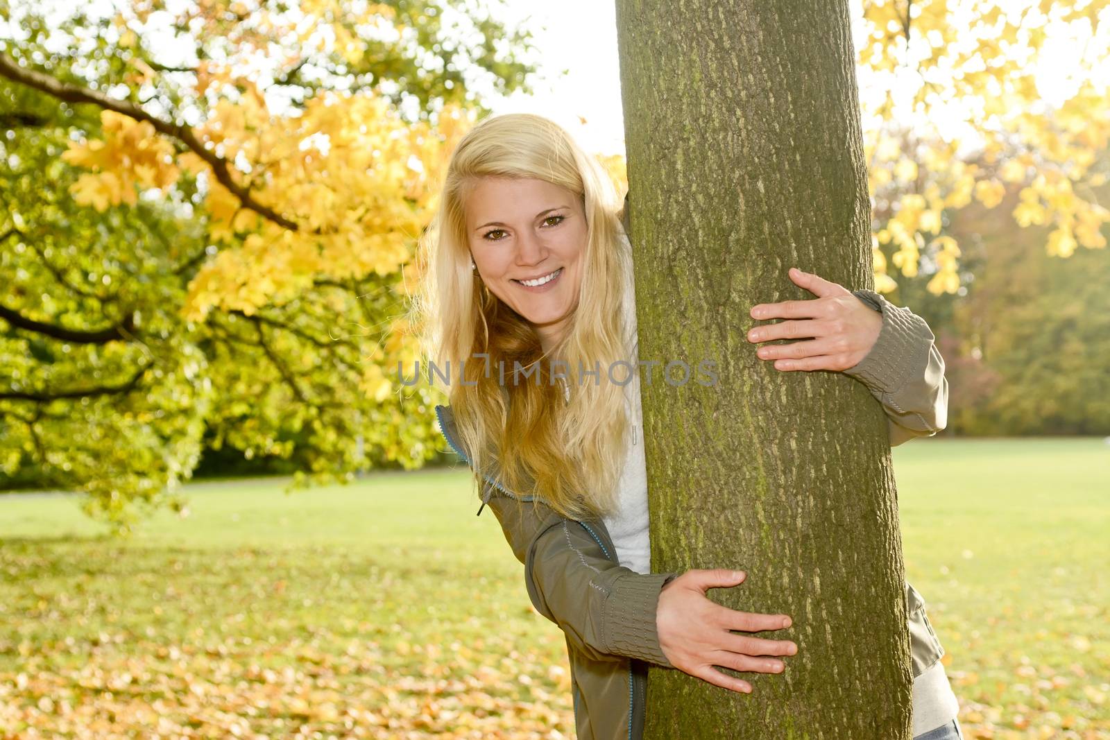 laughing young blond woman hugging a tree in autumn park