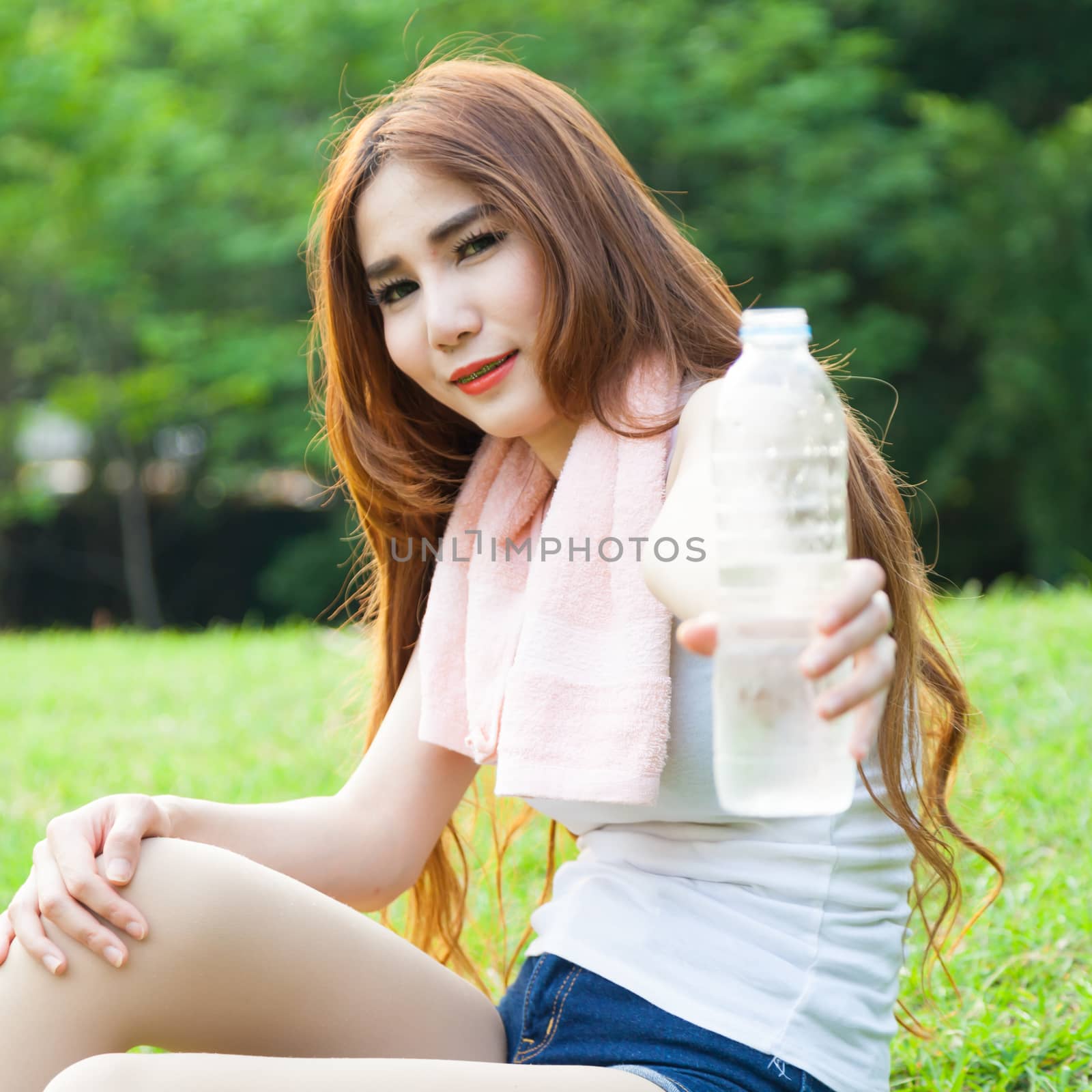Women held a water bottle to drink. Sit on the lawn after exercise in park.