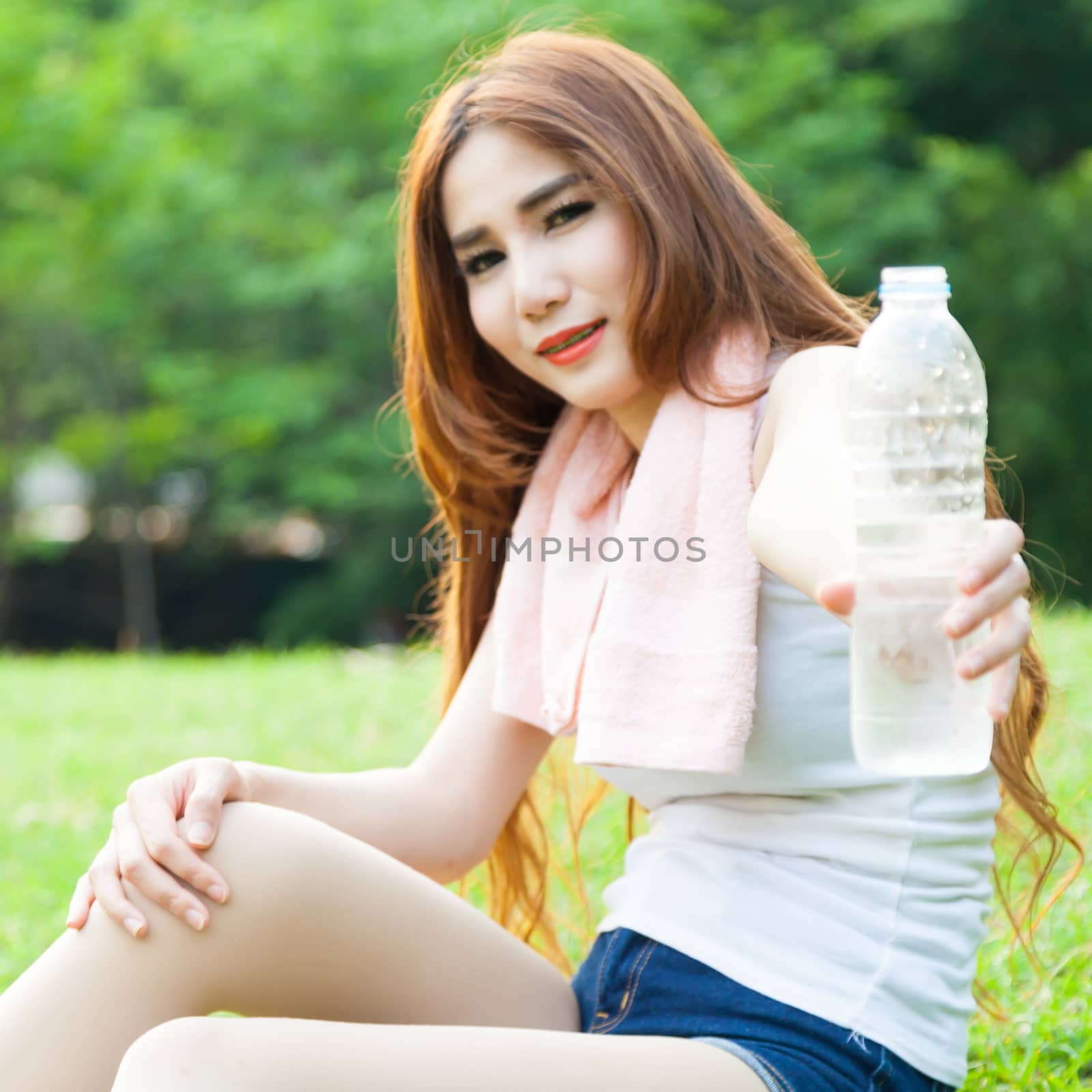 Women held a water bottle to drink. Sit on the lawn after exercise in park.