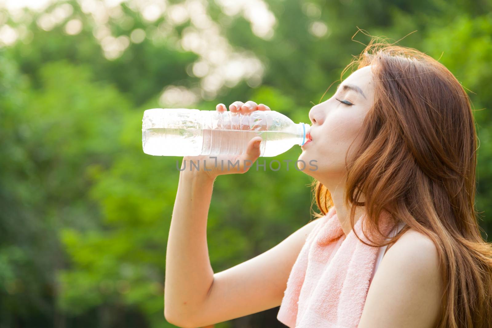 Woman sitting tired and drinking water after exercise. Within the lawn of park.