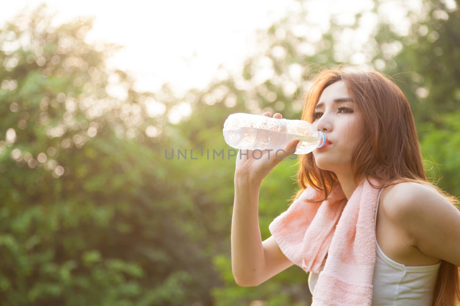 Woman sitting tired and drinking water after exercise. Within the lawn of park.