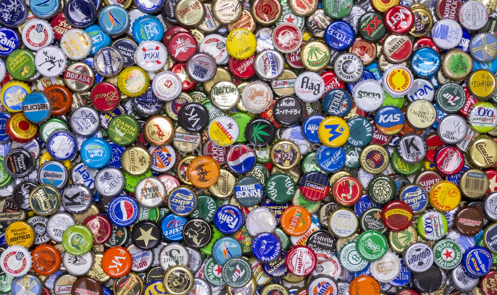 Aerial view of an unordered collection of crowncaps of different brands and types of drink.