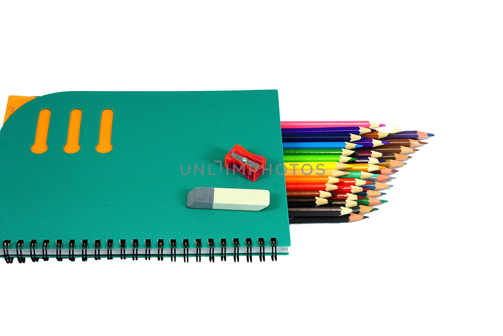 Lie on a white background notebook, sharpener, eraser and lots of colored pencils