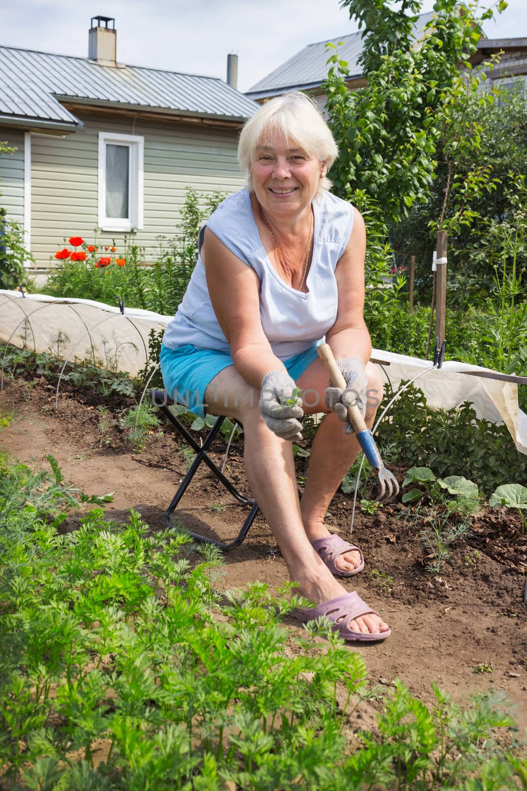 Elderly woman removes the weeds in the garden, sitting on a chair