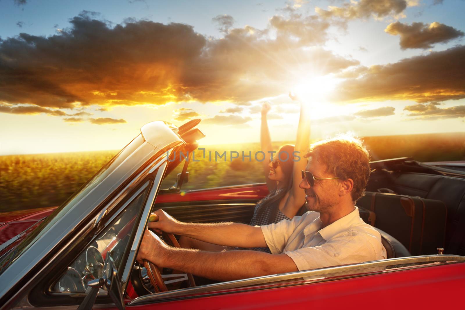 Couple driving convertible car enjoying a summer day at sunset