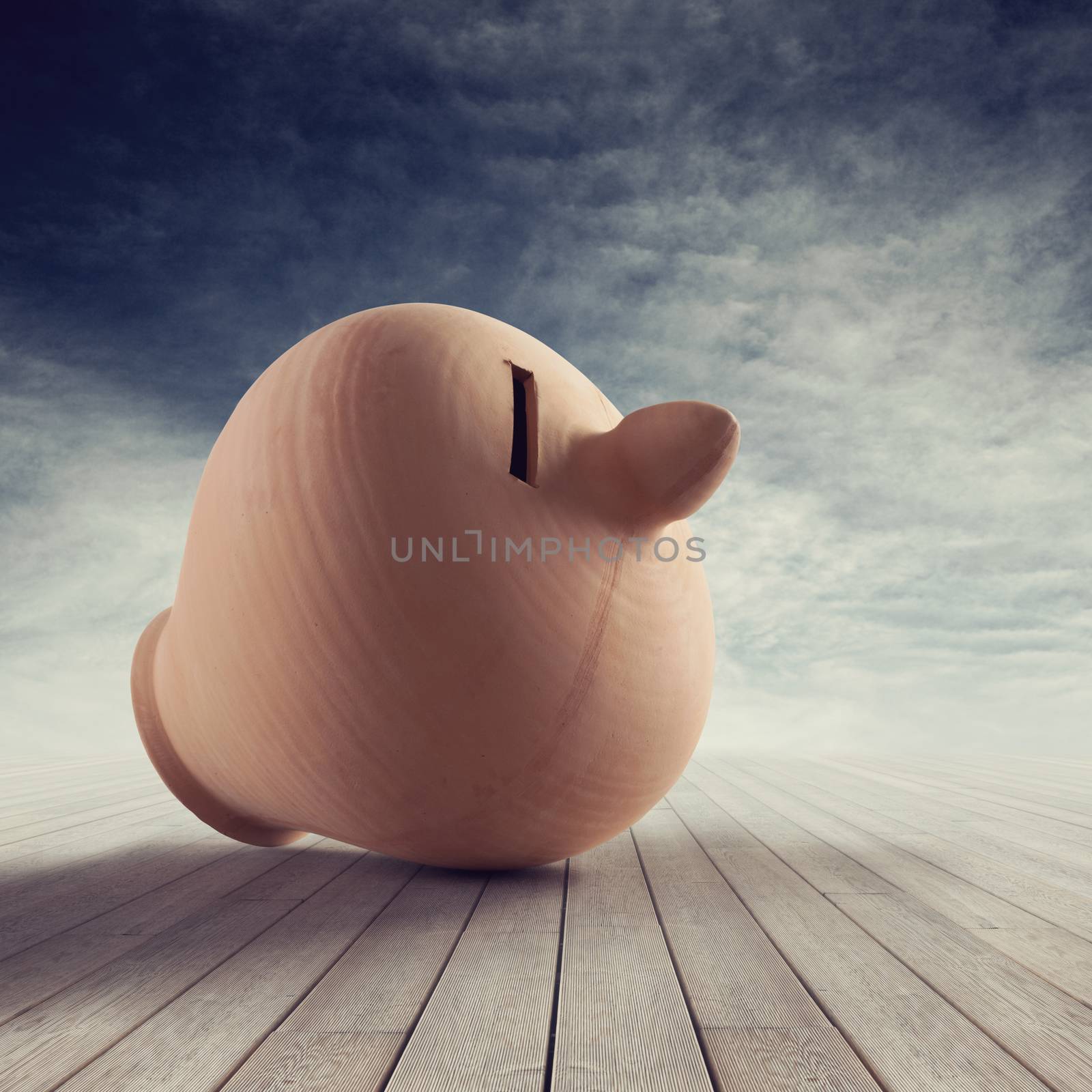 Clay coin bank on wooden plank floor with cloudy sky on background.