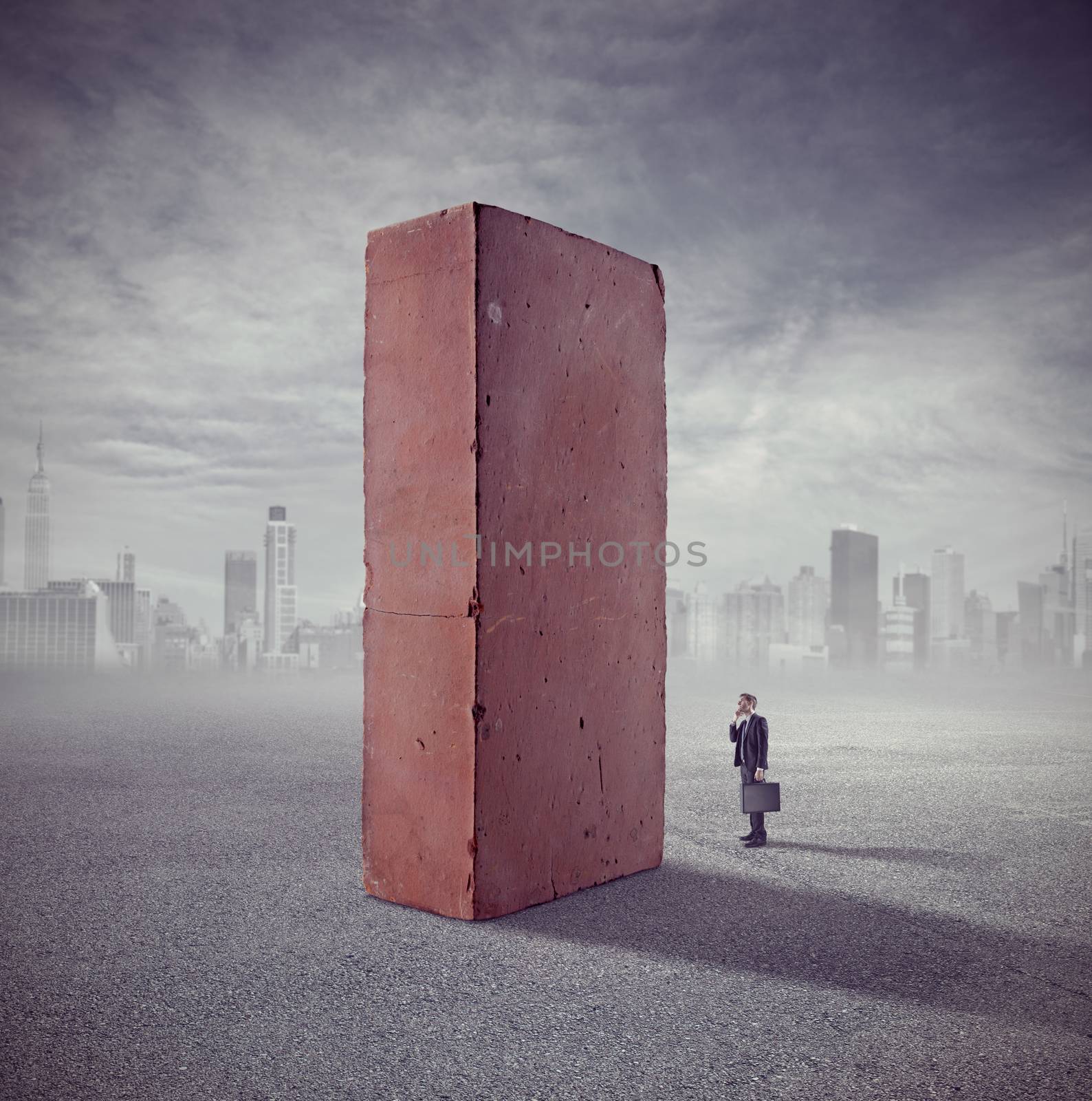 Businessman staring at huge standing brick with skyline and clouds on background.
