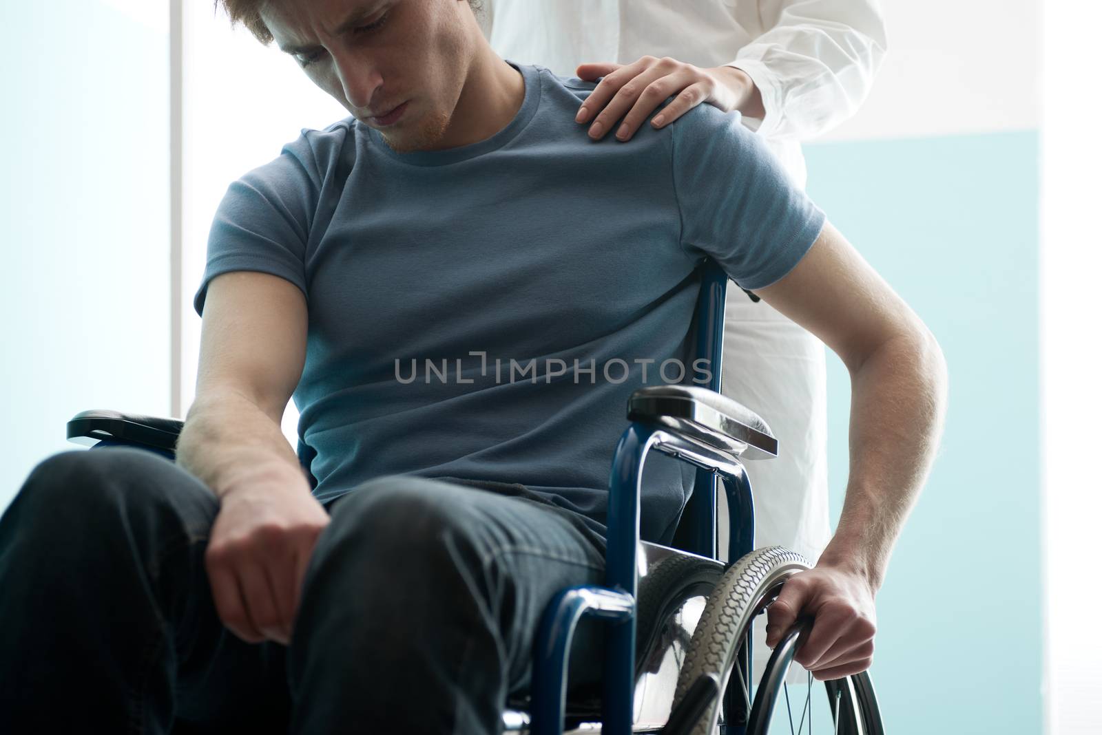 Doctor consoling young man sitting in wheelchair by stokkete