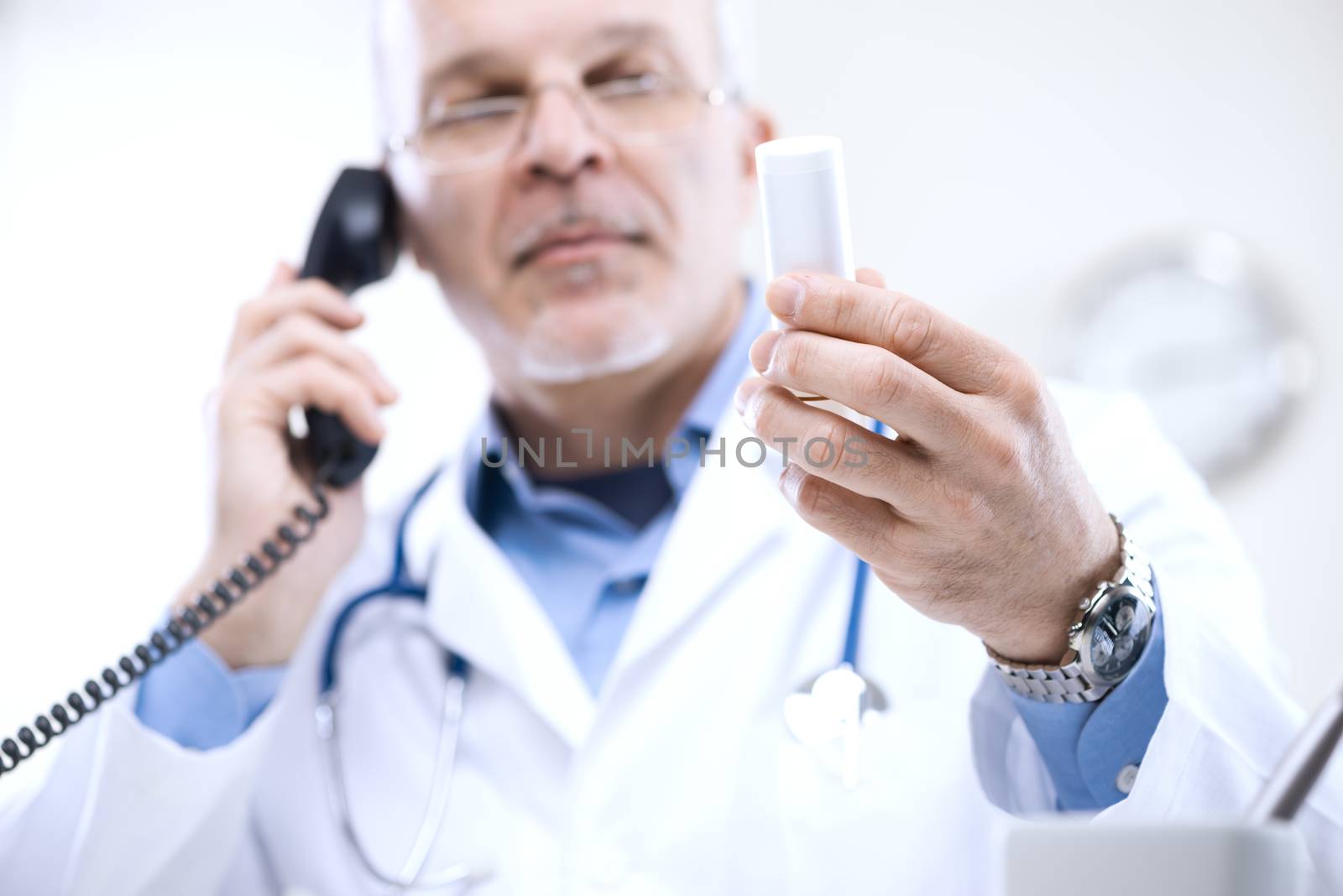 Doctor talking on the phone and looking at medicine's bottle.