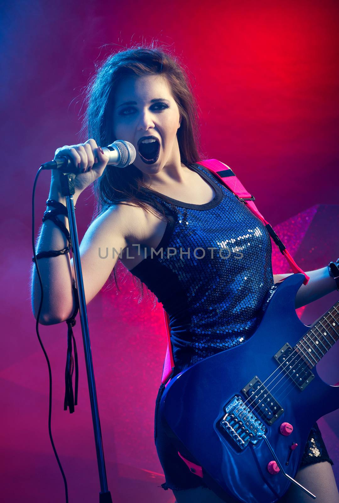 Young teenager rock star singing and playing electric guitar on stage.