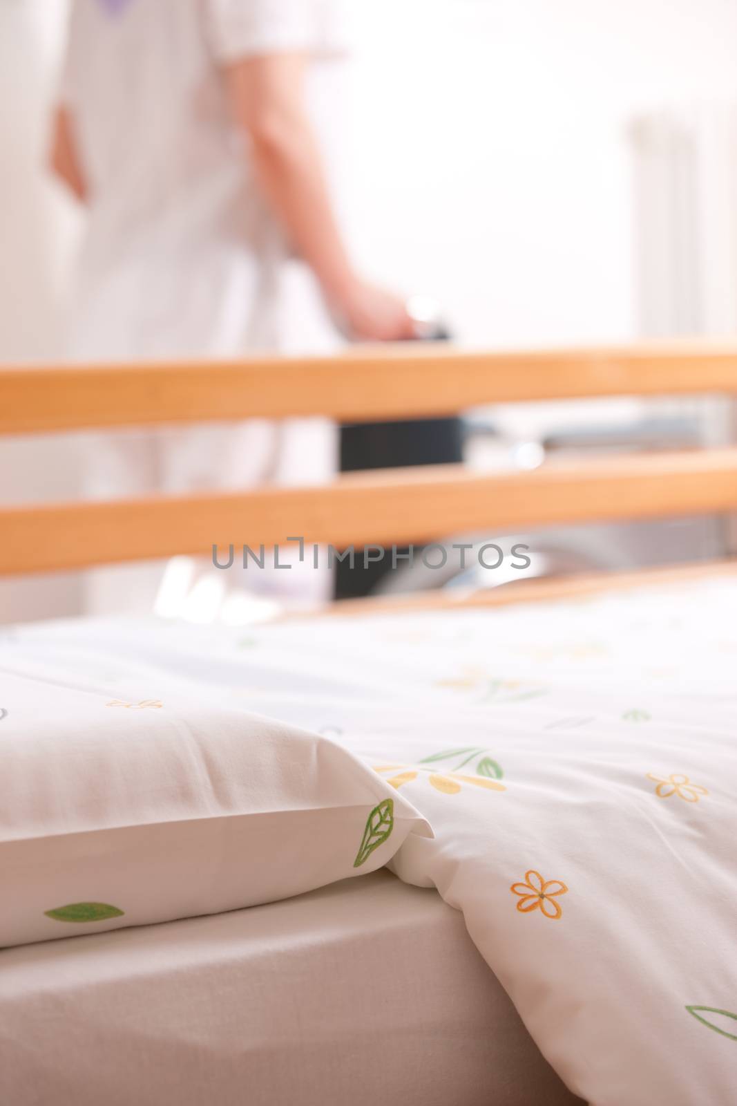 Bed at nursing home with nurse and wheelchair on background.