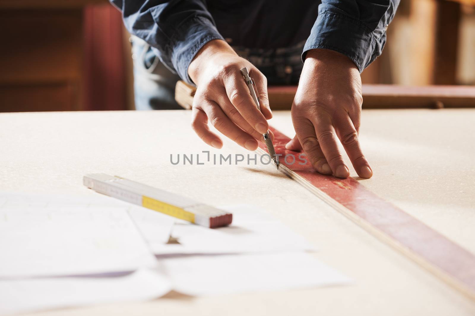 Carpenter measuring and tracing lines with a ruler on a wooden surface.