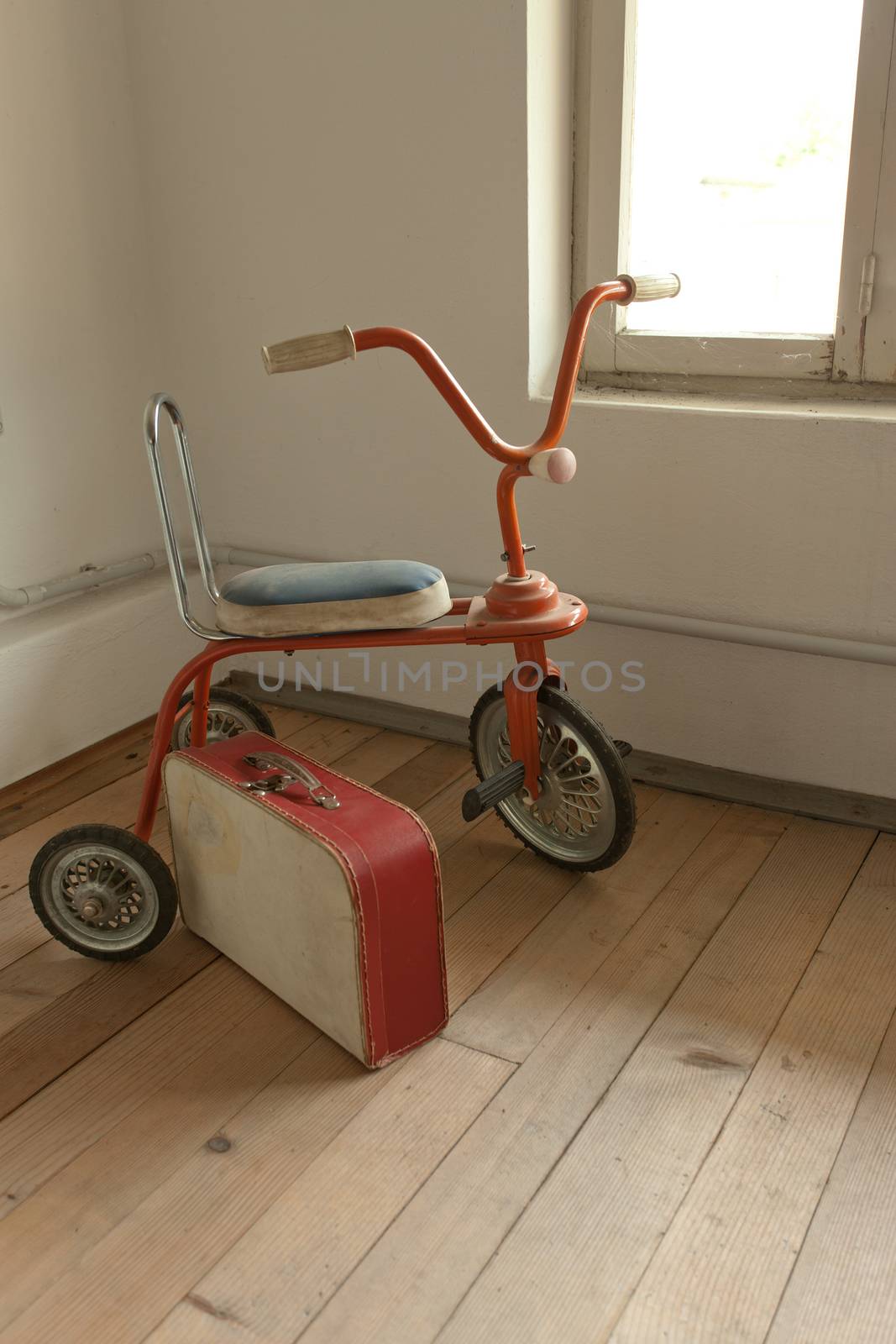 Vintage red tricycle and old suitcase on hardwood floor.