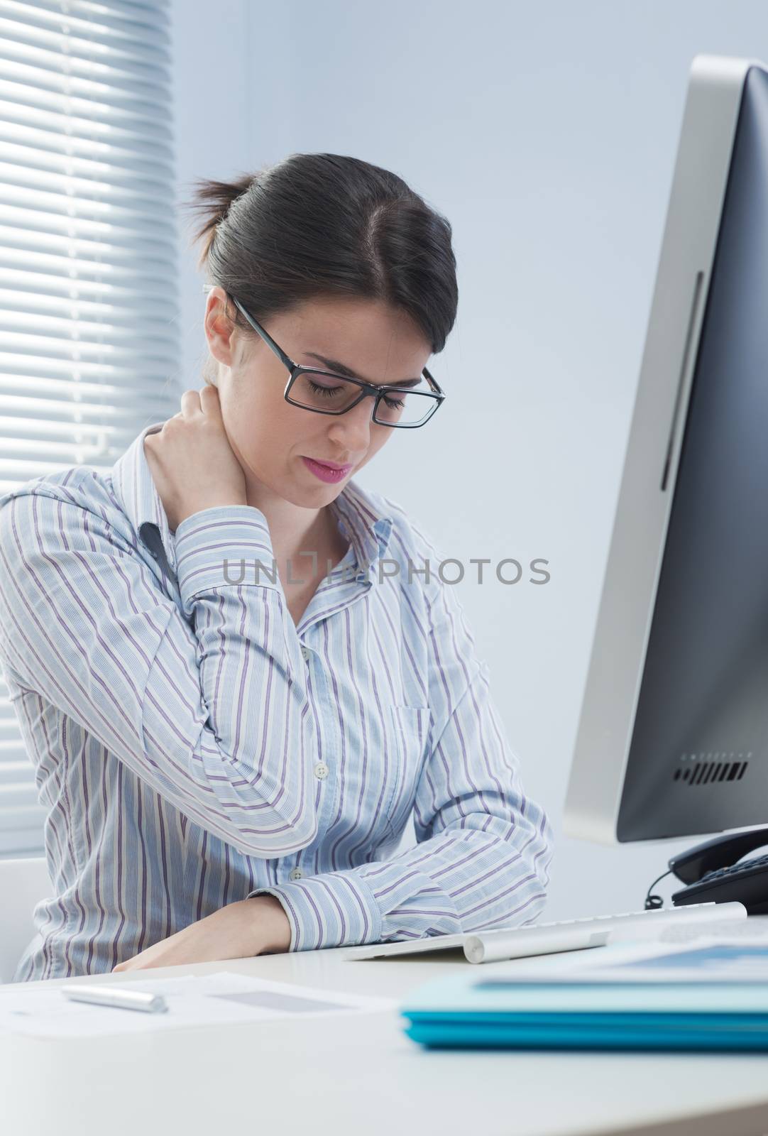 Young office worker with neck pain touching her back.