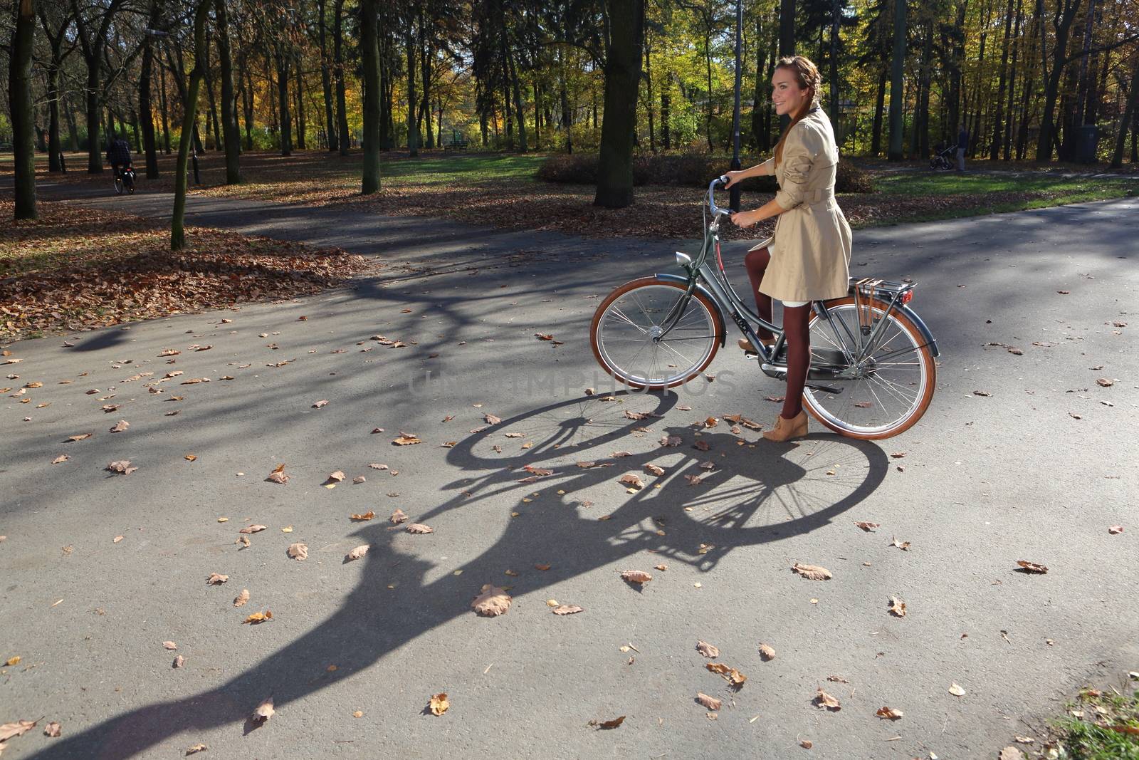 girl on a bicycle in a park alley background color of autumn leaves by robert_przybysz