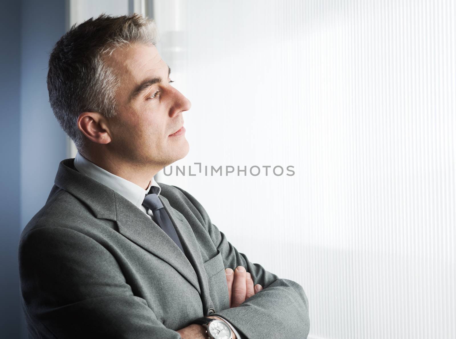 Confident businessman with arms crossed looking through a window.