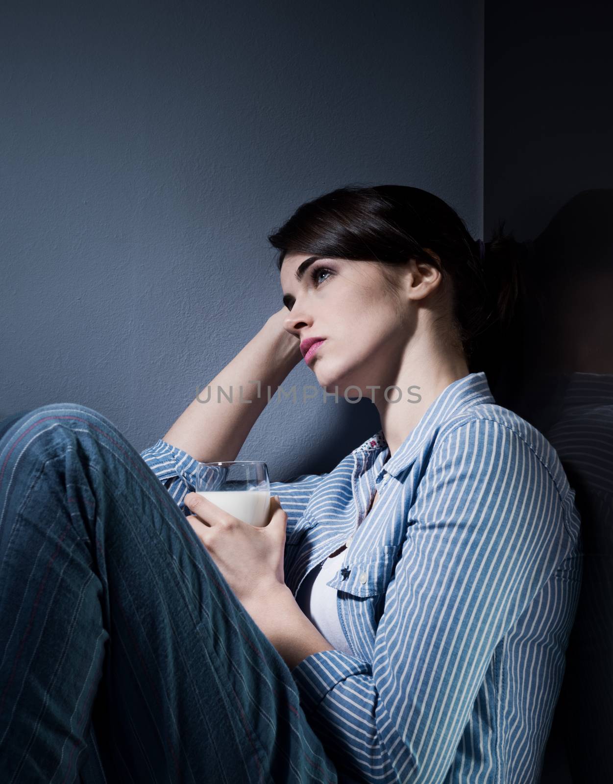 Sleepless sad woman sitting on kitchen floor having a glass of milk.