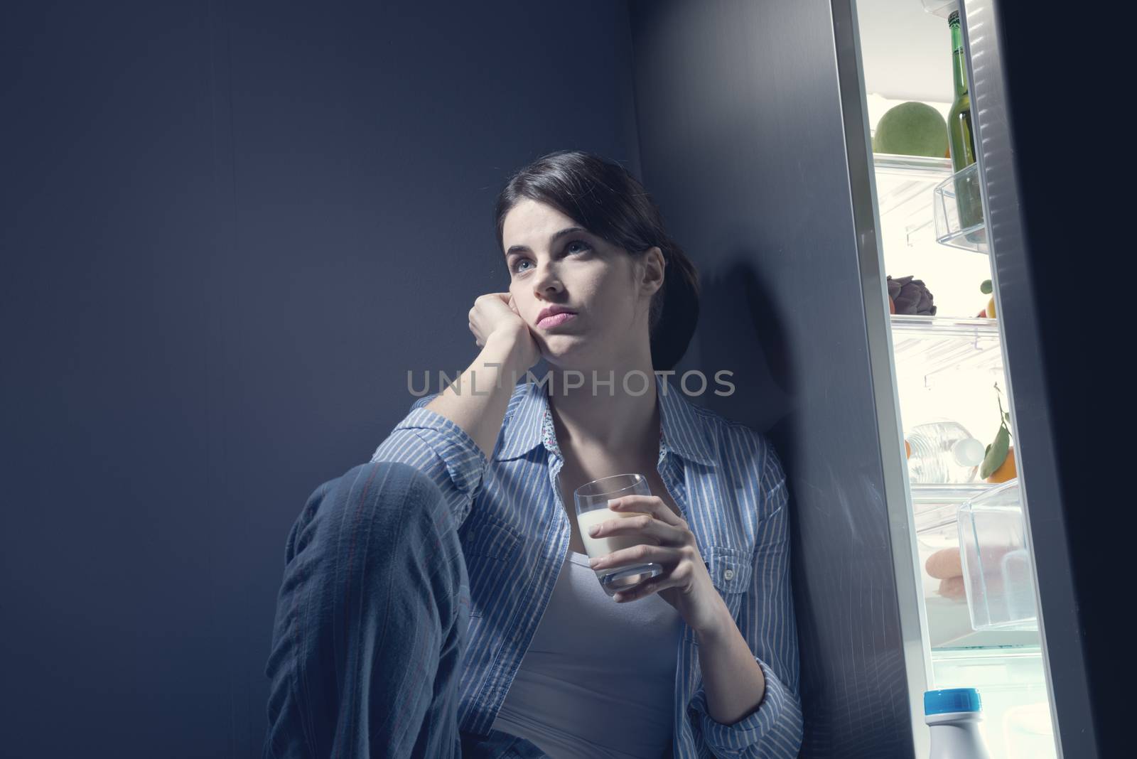 Sleepless sad woman sitting on kitchen floor having a glass of milk.