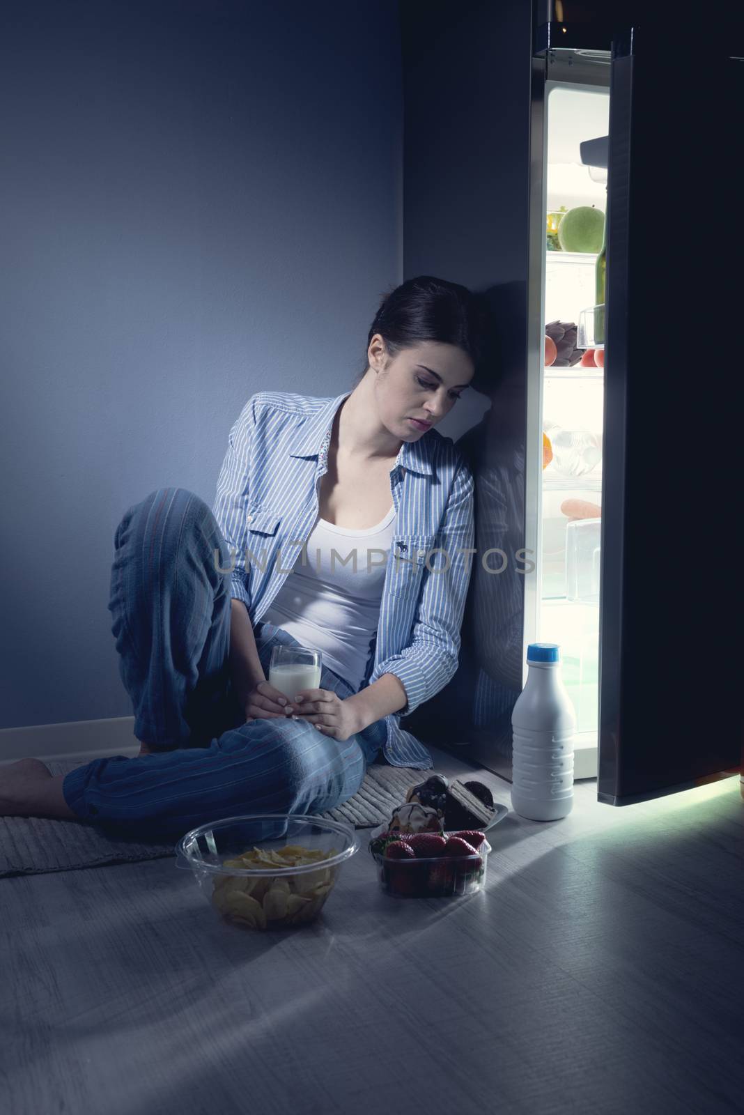 Sleepless sad woman sitting on kitchen floor having a glass of milk.