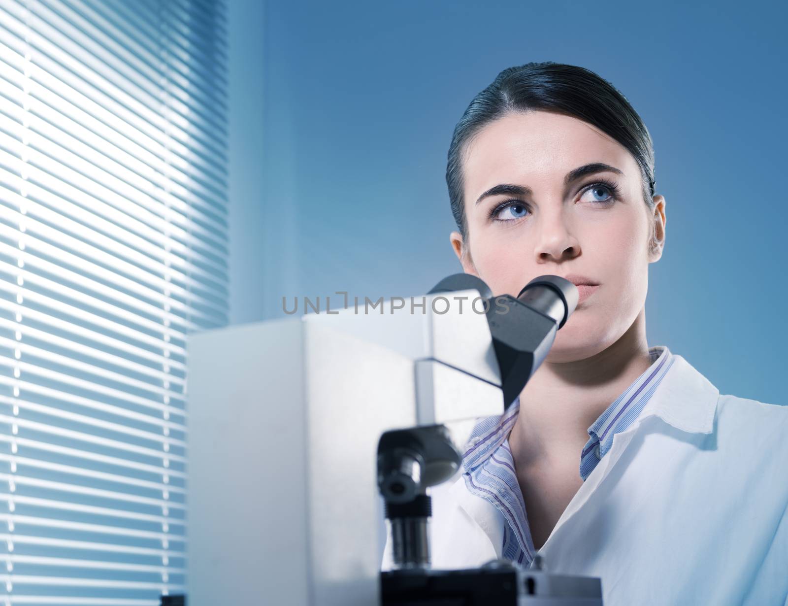 Young female researcher using microscope and thinking in the chemistry laboratory.