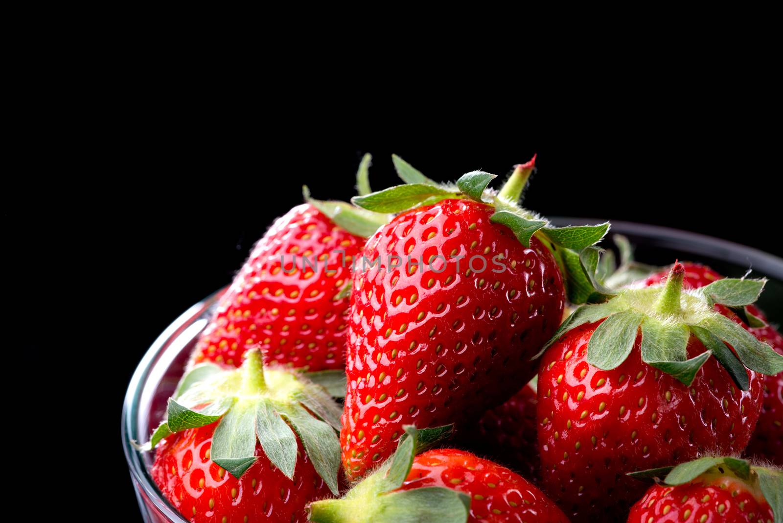 Delicious strawberries in a glass bowl on black background.