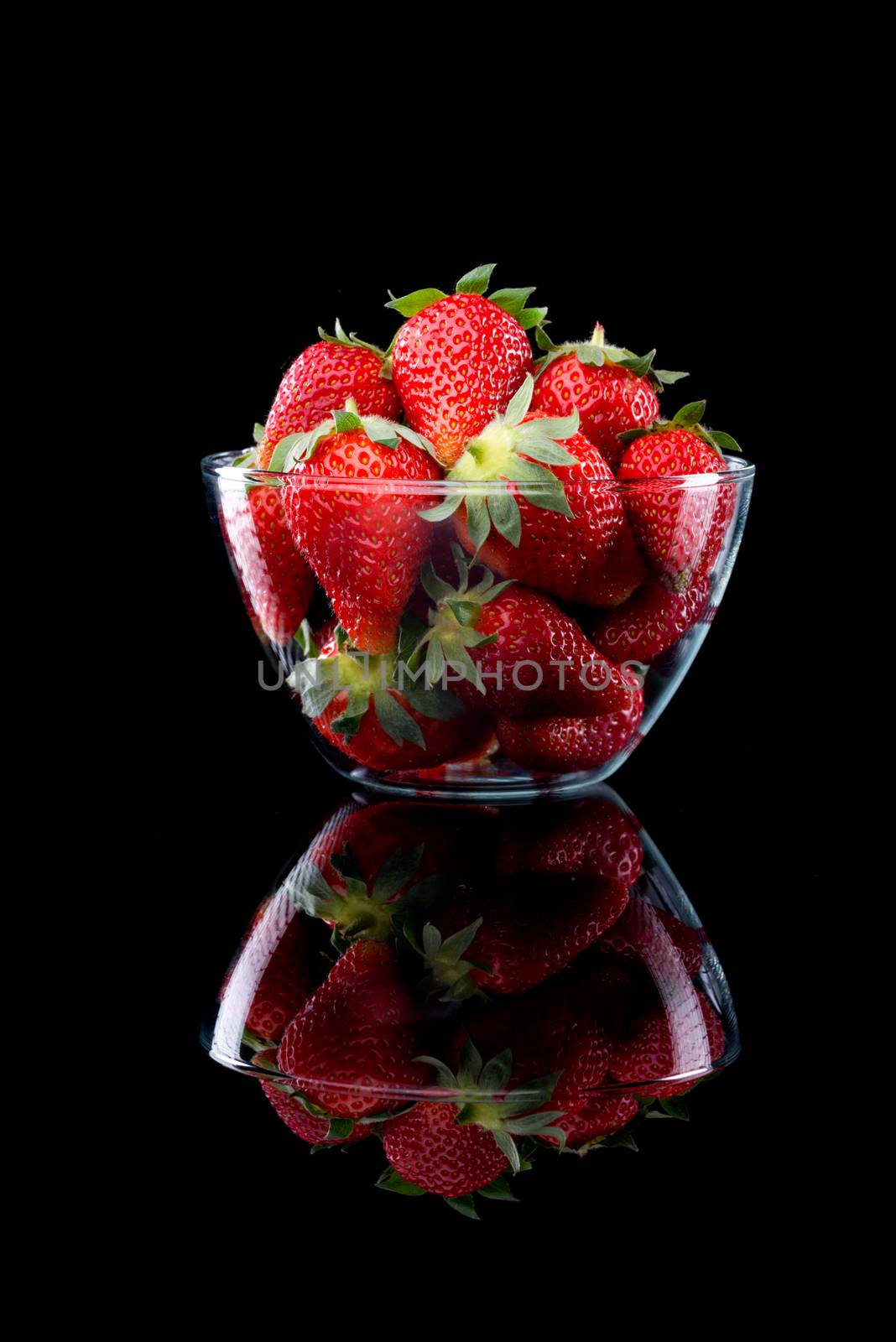 Delicious strawberries in a glass bowl on black background.