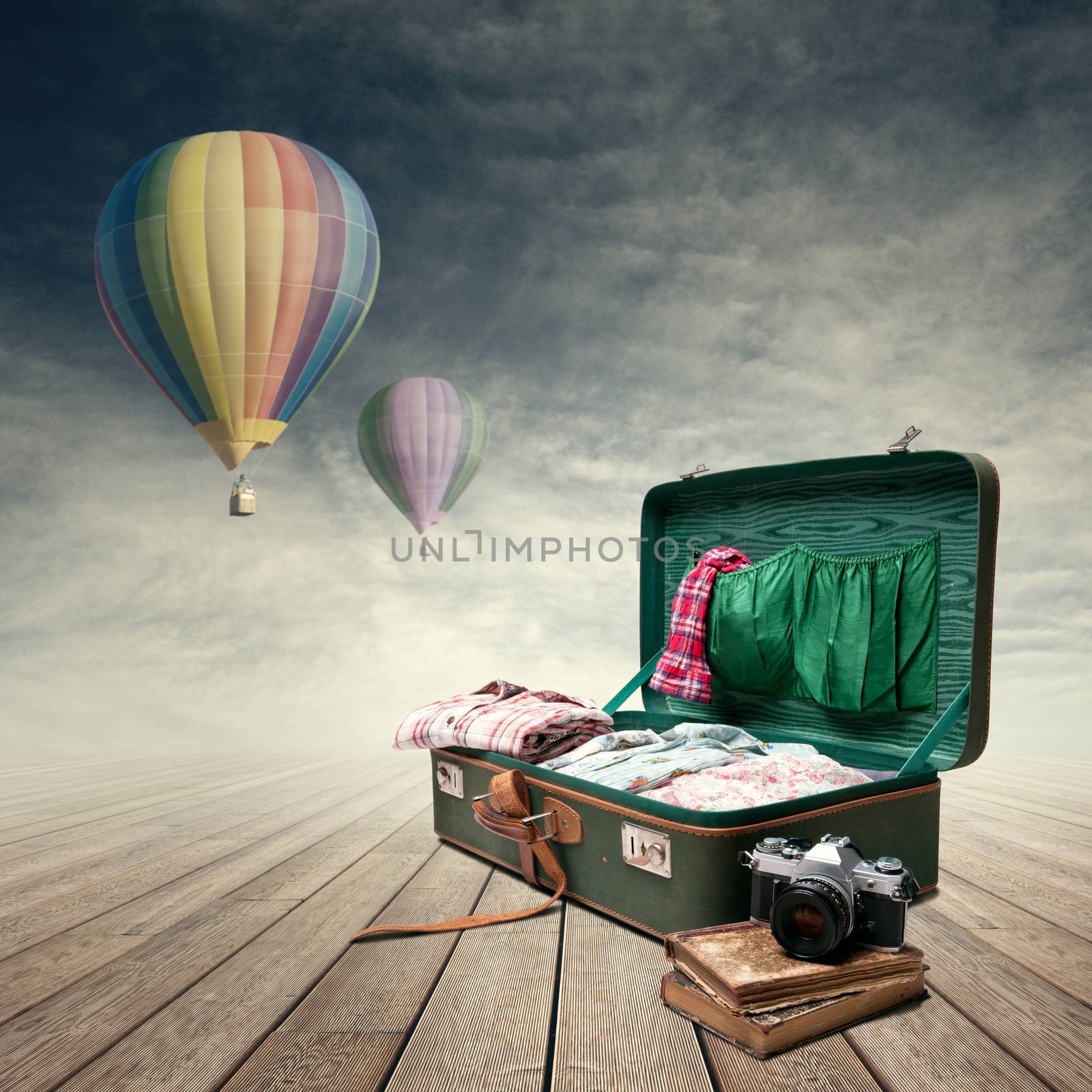 Vintage suitcase with old books and camera, hot air balloons flying on background.