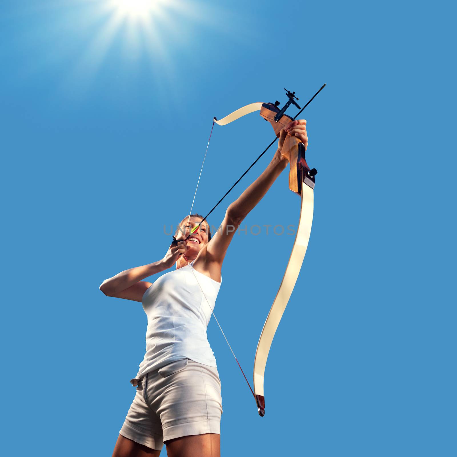 Attractive woman aiming with bow and arrow with blue sky on background.