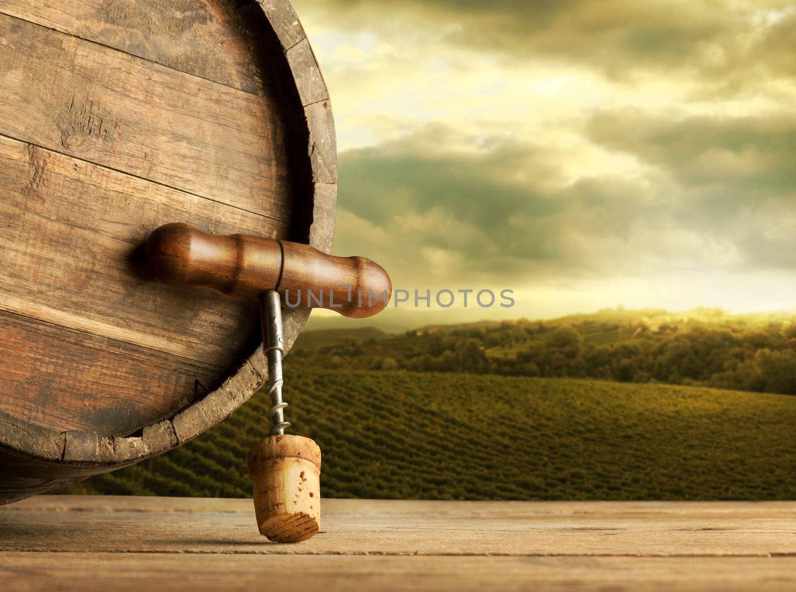 Wooden barrel and corkscrew close up with vineyards and rural landscape on background.