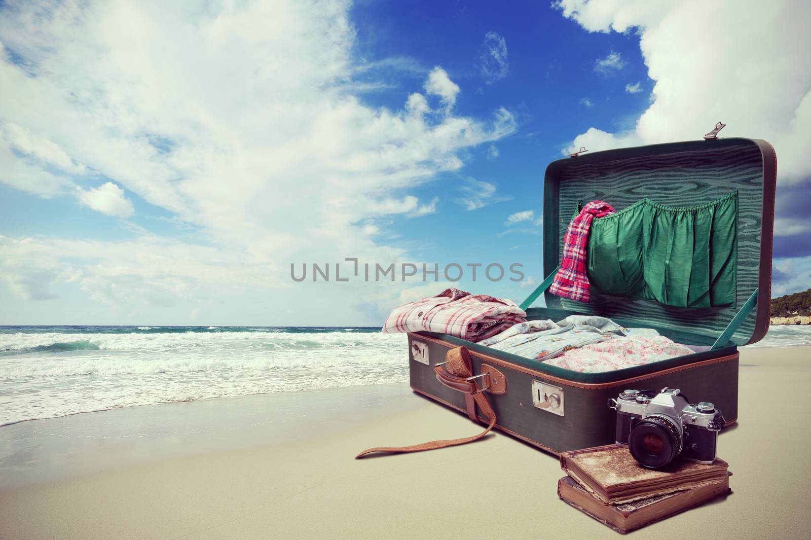 Open suitcase with old books and camera with seaside and blue sky on background.