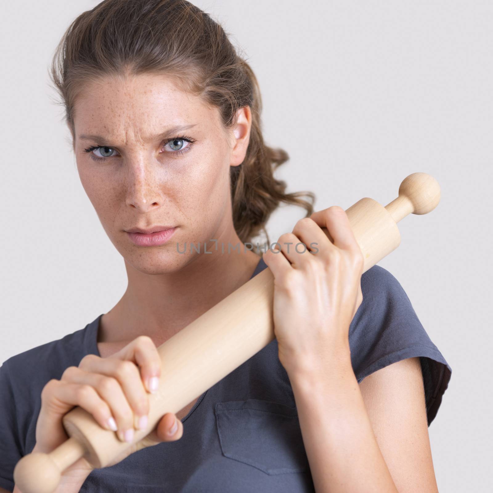 Aggressive woman holding a wooden rolling pin and looking at camera.