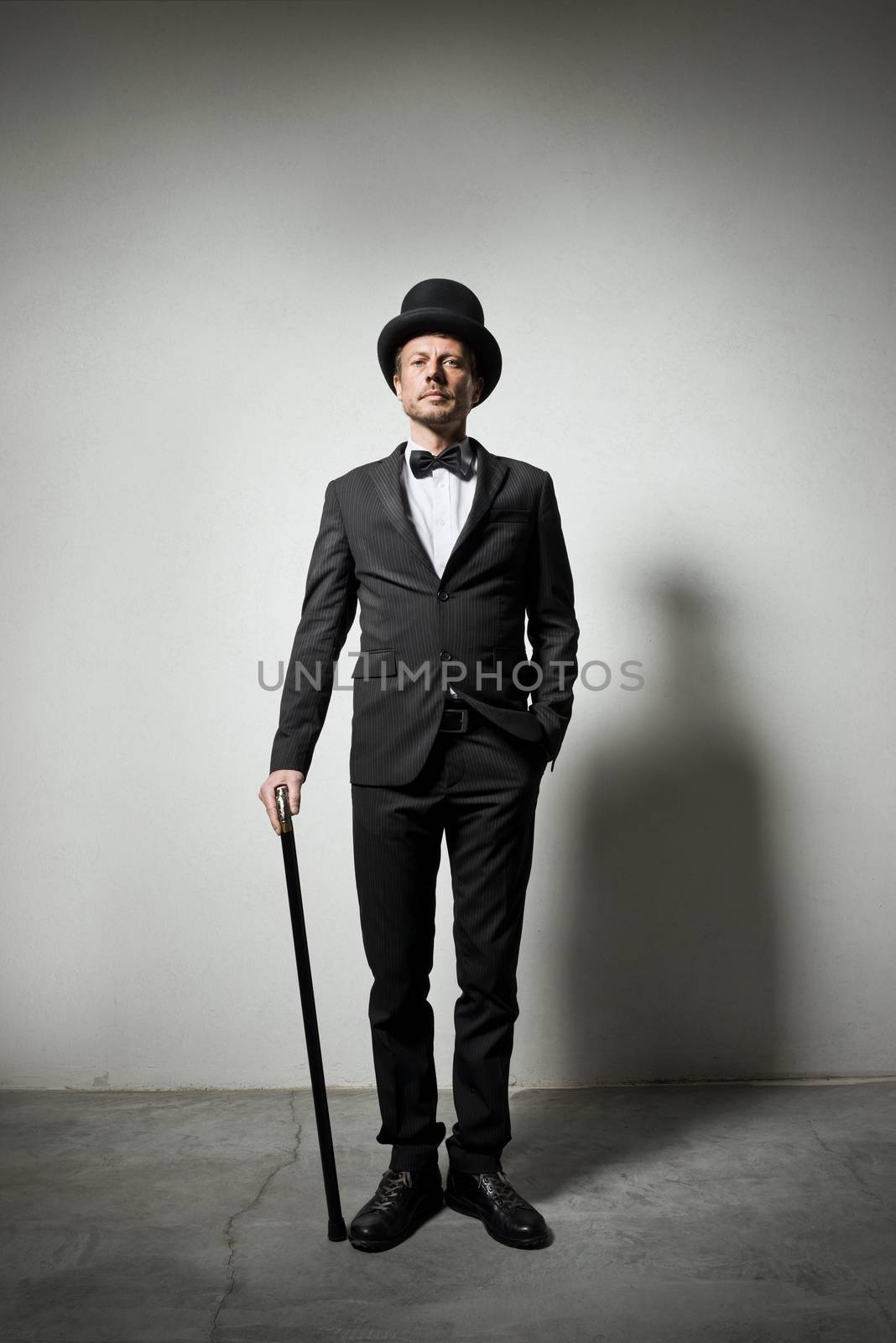 Classy gentleman with bowler hat and cane looking confidently at camera.
