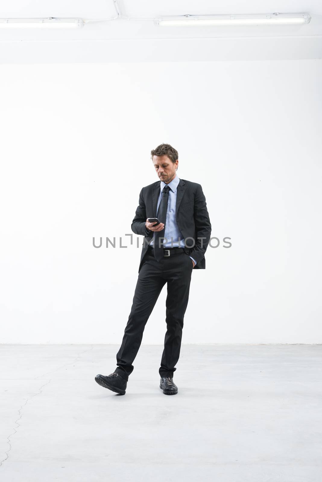 Elegant businessman waiting and texting with mobile phone in an empty room.