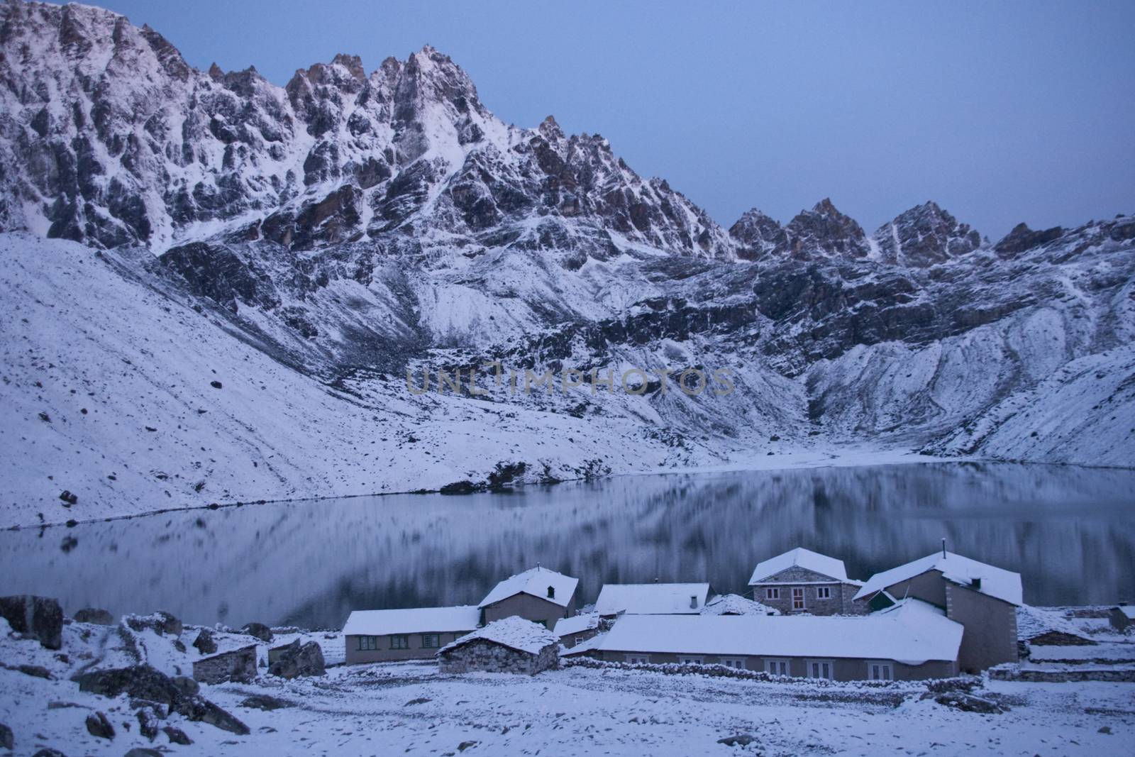 Snow covered buildings in the village of Gokyo next to a still lake and surrounded by mountains 4800 meters up in the Himalaya Mountains of Nepal.