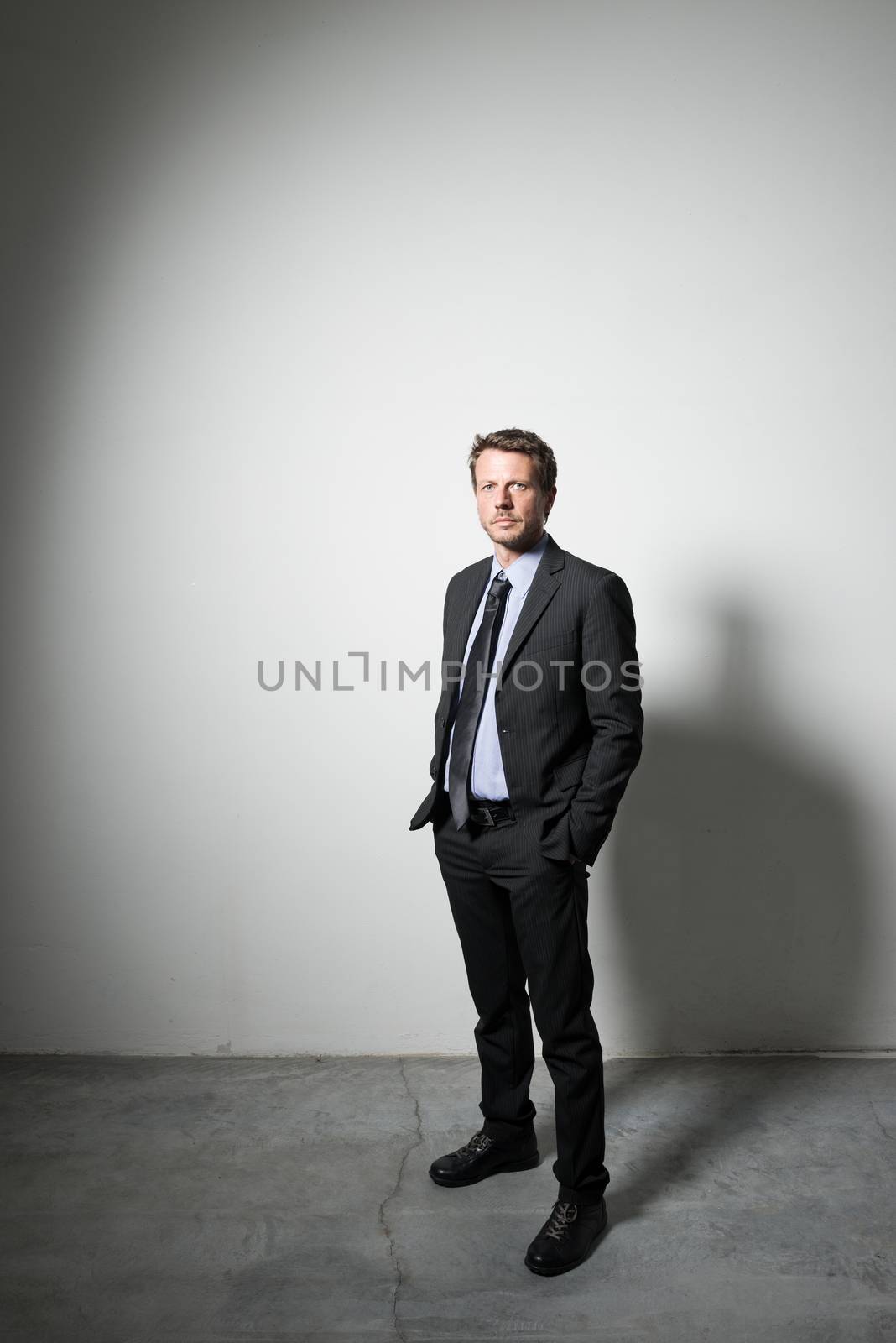 Confident businessman standing with hands in pockets and dramatic lighting.