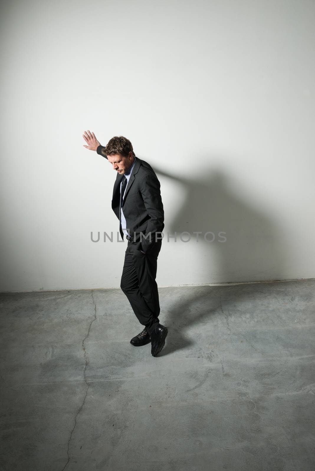 Tired pensive businessman leaning on a wall in an empty room with dramatic lighting.