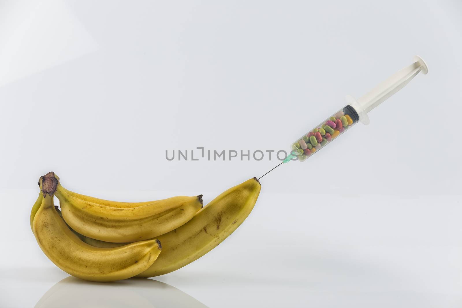 Male impotence metaphor: syringe with pills injecting into a  big banana among small bananas