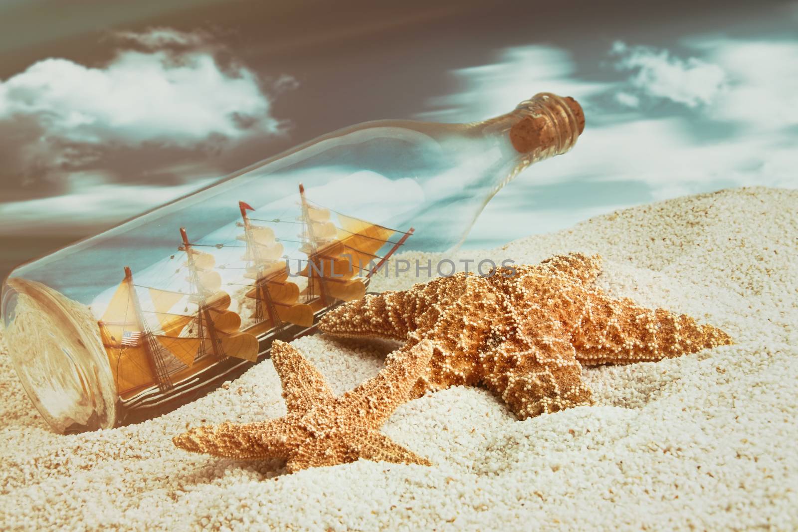 Bottle with ship inside on the beach with starfish