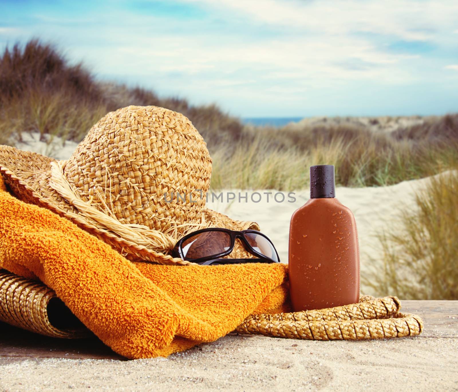 Straw hat with towel and lotion at the beach  by Sandralise